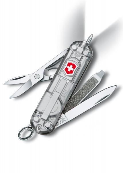 Das Bild zeigt das SilverTech SwissLite Taschenmesser in Silber mit transparenter Hülle und LED. Es enthält verschiedene Werkzeuge, darunter eine Schere, eine Feile und ein Messer. Der Griff ist mit dem roten Schweizer Kreuz-Logo versehen. Die transp