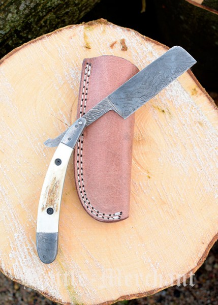 Ein elegantes Damast-Rasiermesser mit einem Griff aus Hirschhorn und einer scharfen Klinge, das auf einem Holzblock neben einem Lederetui liegt. Die exquisite Handwerkskunst des Messers spiegelt sich in den Details wider.